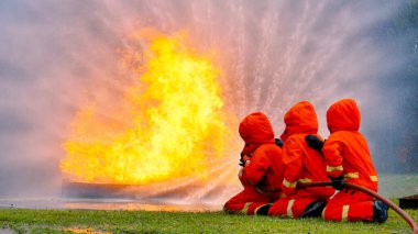 Firefighter Rescue team training in fire fighting extinguisher. Firefighter teamwork fighting with flame using fire hose chemical water foam spray engine. Fireman wear hard hat, safety suit uniform