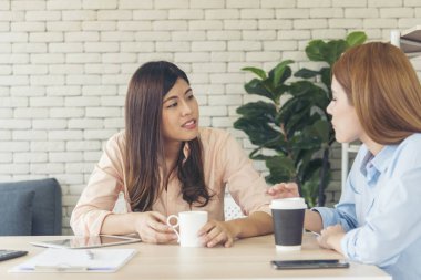İki bayan meslektaşım ofis masasında kahve fincanı içiyorlar. Asyalı bir kadın arkadaşça sinsice gülüyor. Takım çalışması mutlu an yaşam tarzı. Uluslararası Kadın Günü konsepti