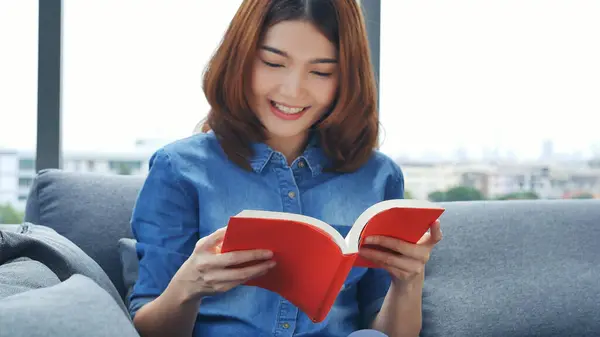 Relax asian woman reading book sitting on sofa in living room holding book to read. Young woman relaxation reader reading open book leisure mind. Happiness beauty woman person smiling face happy time