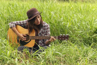 Yeşil parkta akustik gitar çalan genç kadınlar. Evde akustik gitar enstrümanı çalan bir kadın, güzel doğada genç Asyalı müzisyen kız yaşam tarzı. Mutlu gitarist
