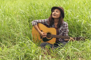 Yeşil parkta akustik gitar çalan genç kadınlar. Evde akustik gitar enstrümanı çalan bir kadın, güzel doğada genç Asyalı müzisyen kız yaşam tarzı. Mutlu gitarist