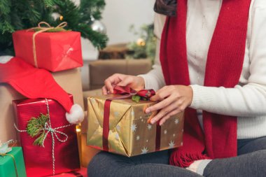 Kadın eli hediyesini sıcak oturma odasına sarın. Noel ağacının altında hediye paketi yapan bir kadın. Asyalı kadın dekoratif balo balosu Noel ağacı Noel 'de kış mevsimi kutlamalarında