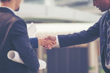 İnşaat mühendisi takımları el sıkışırken inşaat alanında kask takıyor. Foreman Endüstri Projesi Mühendis ekip çalışması. İki Asyalı mühendis takımı el sıkışıyor.