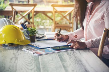 İnşaat mühendisi kadın, ofis masasında dizüstü bilgisayarla çalışıyor. Beyaz, inşaat ofisinde sarı kasketli. Asyalı genç adam mimarlık projesi yöneticisi ofiste oturuyor.