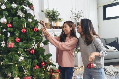 Noel ağacı süslemesi yapan iki kadın kardeş. Kırmızı top, takı, kar tanesi. Kırmızı topu tutan elleri kapatın. Mücevher süsleme. Asyalı kadın arkadaşlar, dekorasyon balosu, Noel ağacı, Noel tatili.
