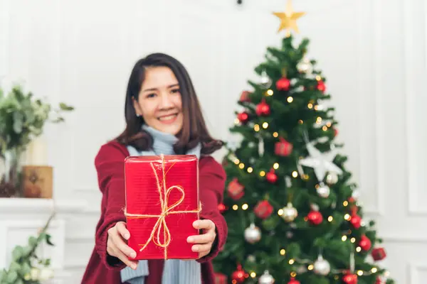 Woman surprise got present gift box on christmas eve. Asian woman holding christmas gift box under xmas tree with smiling face. Woman hands wrap present gift. Merry christmas happy new year concept