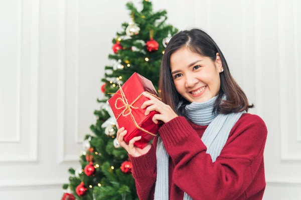 Woman surprise got present gift box on christmas eve. Asian woman holding christmas gift box under xmas tree with smiling face. Woman hands wrap present gift. Merry christmas happy new year concept