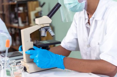 Indian Scientist man look into Microscope research in science laboratory. Asian biochemistry scientist using microscope in laboratory chemistry labs. Covid-19 medical research scientific experiment