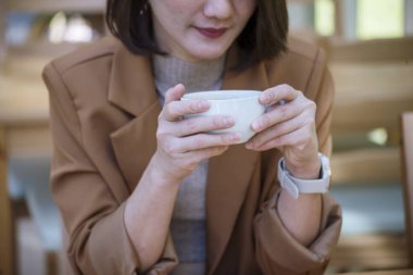 Green Garden Cafe 'de elinde siyah kahve fincanı olan bir kadın. İş kadınlarının elleri sıcak kahve içmeye bayılır. Kahveli iş kadınları ya da kahve dükkanında sıcak çikolata. Kafein içmek