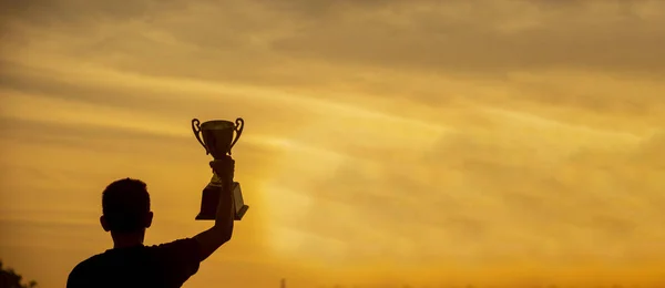 バナー受賞者は金のチャンピオントロフィーカップ賞を保持手を獲得 Silhouette最高の賞の手チャンピオントロフィー パノラマチームは金のスポーツトロフィーカップを保持 コピースペースとWin Winスポーツチーム ロイヤリティフリーのストック画像