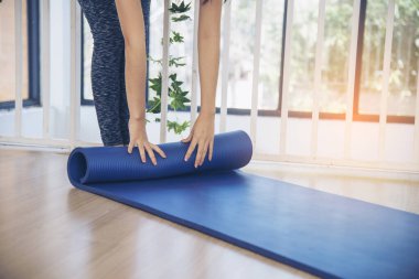 Kadın elleri yoga antrenman odasında jimnastik zemininde yoga minderini sardı. Egzersiz yapan kadın, köpüklü yoga paspası saran elleri kapıyor. Kadın yalınayak evde spor yapıyor sağlıklı yaşam tarzı konsepti