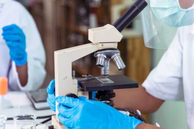 Indian Scientist man look into Microscope research in science laboratory. Asian biochemistry scientist using microscope in laboratory chemistry labs. Covid-19 medical research scientific experiment