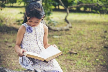 Doğal bahçedeki yeşil parkta kitap okuyan Asyalı kız. Genç kız rahatlama açık kitap kişisel çalışma okudu. Mutlu çocuk kadınlar mutlulukla gülerek öğreniyor. Çocuk yeşil parkta oturuyor.