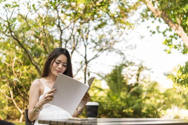 Green Park 'ta elinde kitap okuyan Asyalı bir kadın. Genç kadın rahatlama açık kitap kişisel çalışma okudu. Üniversiteli kadınlar mutluluktan gülümsüyor. Kadınlar yeşil parkta oturuyor.