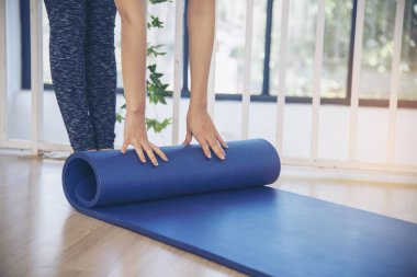 Home workout woman close up hands rolling foam yoga gym mat. Woman hands rolled up yoga mat on gym floor in yoga fitness training room. Woman barefoot home workout sportive healthy lifestyle concept