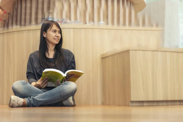 Asian woman holding book reading at bookshelf in university library. Young woman relaxation read open book self study. University women self study at library bookstore. Education learning knowledge