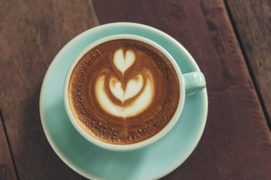 Sütlü, ahşap masadaki Latte sanat kahve fincanı. Espresso shot 'la sütlü kahve fincanı yapılır. İtalyan kafeteryasında sütlü kapuçino. Kafeteryada fotokopi alanı olan kahverengi kahve içeceği.