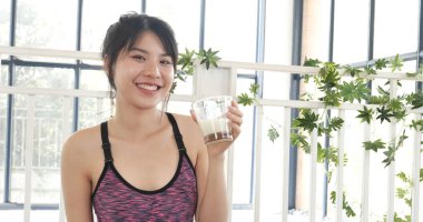 Kadın elleri şişeden akan beyaz süt bardağını tutuyor. Asyalı kadınlar güler, kameralı sağlık hizmetleri yaşam tarzına bakarlar. Güzel bayan az yağlı süt içen laktozsuz süt.