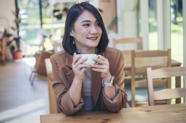 Kahve dükkanında elinde taze fincanla sade kahve içen güzel kadın. Kahve sever. Asyalı kadın, yeşil bahçe kafesinde elinde fincanla sade kahve içiyor. Genç kadın gülümse aşkım, kahve iç.