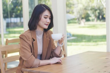 Kahve dükkanında elinde taze fincanla sade kahve içen güzel kadın. Kahve sever. Asyalı kadın, yeşil bahçe kafesinde elinde fincanla sade kahve içiyor. Genç kadın gülümse aşkım, kahve iç.