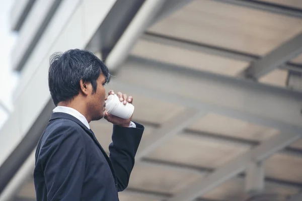 Businessman drinking coffee cup relax at office desk working with smart tablet computer laptop. Asian man work at office warm taste in cafe. Close up man hands sitting holding black coffee cup