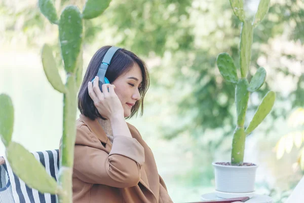 Happy asian woman use headphones listen to music from smartphone outdoor in green park nature. Music mental therapist for relaxation woman. Leisure cheerful wellness woman smile sitting in green park