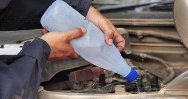 Araba tamircisi elleri araba aküsü mekanik servisi için arıtılmış arıtılmış su döküyor. Kapatın elleri adamım. Deiyonize edilmiş sıvı su şişesini garajdaki mobil araba servisinde tutun.