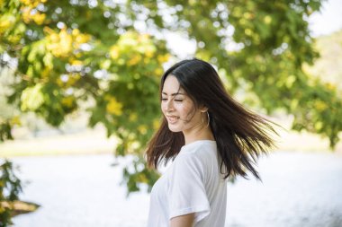 Happy sakin ol güzel Asyalı kadın gülümseyen yüz yeşil parkın bahçesinde duruyor. Genç kadınlar sabah Özgürlük Yaşam tarzının tadını çıkarıyorlar. Kadın temiz hava soluyor ve yeşil parkta nefes alıyor.