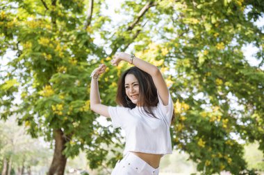 Happy sakin ol güzel Asyalı kadın gülümseyen yüz yeşil parkın bahçesinde duruyor. Genç kadınlar sabah Özgürlük Yaşam tarzının tadını çıkarıyorlar. Kadın temiz hava soluyor ve yeşil parkta nefes alıyor.