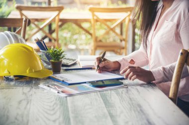 İnşaat mühendisi kadın, ofis masasında dizüstü bilgisayarla çalışıyor. Beyaz, inşaat ofisinde sarı kasketli. Asyalı genç adam mimarlık projesi yöneticisi ofiste oturuyor.