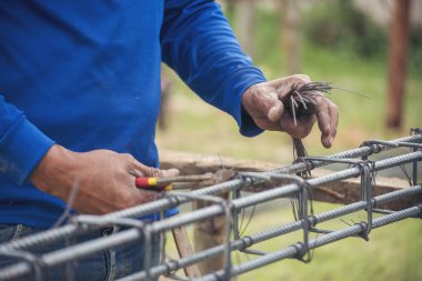 Erkeklerin elleri beton işçiliğini güçlendirmek için kerpeten kullanıyor. İnşaat işçisi elleri çelik tel örgüleri keserek büküyor. Açık hava işçisi, tel bükme pensesi kullanıyor, inşaat işi yapıyor..