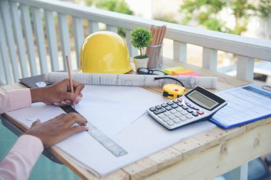 İnşaat mühendisi, ofis binasında dizüstü bilgisayarla beyaz sarı kasketli inşaat alanında çalışıyor. Asyalı genç adam mimarlık projesi yöneticisi ofiste oturuyor.