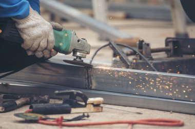 İnşaat işçisi elleri kaynak makineleri ile metal kıvılcımlar saçıyor. Erkek elleri koruyucu eldiven giyer. Alev metali, ateş demiri atölyesini keser. Çilingir kaynak makinesi kullanarak metal işlemini kesti
