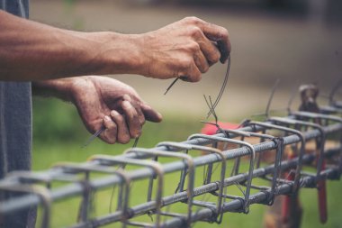 İnşaatçıların elleri çelik telleri büküyor beton işçiliğini destekliyor. Kerpeten kullanan işçi elleri demir tel kullanıyor. Açık hava işçisi, tel bükme pensesi kullanıyor, inşaat işi yapıyor.