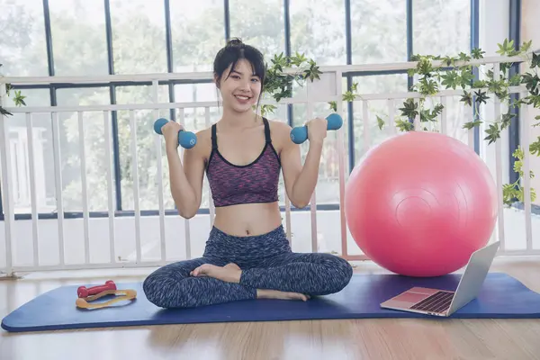 Beautiful Asian Women use dumbbell exercises for muscle-building home fitness. Women weight training smile use exercise pilates ball dumbbell. Beauty woman smiling sportswear on yoga mat home fitness