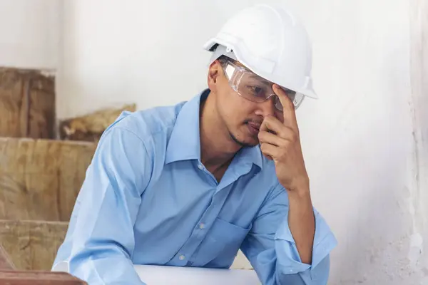 Asian young engineer man stress and failure in architecture project sitting at office on construction site. Upset despair civil construction engineer working on laptop with stressed problems
