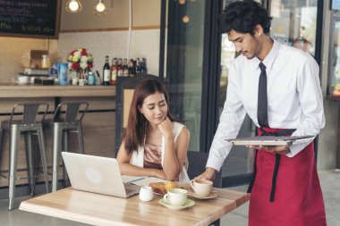 Restoran işi yakışıklı garson gülen yüzlü güzel kadınlara yemek servisi yapıyor. İş kadını, Luch zamanı çalışırken bilgisayar kullanıyor. Garson kafede kahve servisi yapıyor.