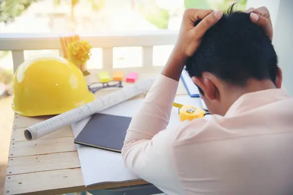 Asian young engineer man stress and failure in architecture project sitting at office on construction site. Upset despair civil construction engineer working on laptop with stressed problems