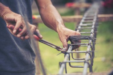 Erkeklerin elleri beton işçiliğini güçlendirmek için kerpeten kullanıyor. İnşaat işçisi elleri çelik tel örgüleri keserek büküyor. Açık hava işçisi, tel bükme pensesi kullanıyor, inşaat işi yapıyor..