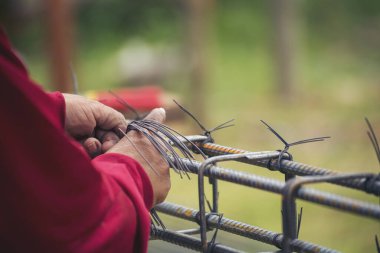 Erkeklerin elleri beton işçiliğini güçlendirmek için kerpeten kullanıyor. İnşaat işçisi elleri çelik tel örgüleri keserek büküyor. Açık hava işçisi, tel bükme pensesi kullanıyor, inşaat işi yapıyor..