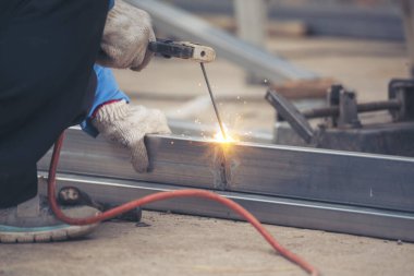 İnşaat işçisi elleri kaynak makineleri ile metal kıvılcımlar saçıyor. Erkek elleri koruyucu eldiven giyer. Alev metali, ateş demiri atölyesini keser. Çilingir kaynak makinesi kullanarak metal işlemini kesti