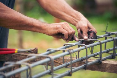 Erkeklerin elleri beton işçiliğini güçlendirmek için kerpeten kullanıyor. İnşaat işçisi elleri çelik tel örgüleri keserek büküyor. Açık hava işçisi, tel bükme pensesi kullanıyor, inşaat işi yapıyor..