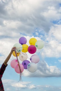 Balon tutan neşeli güzel kadın yeşil parktaki büyük ağacın altında mutlu mesut oturuyor. Kadın Eller 'in elinde canlı hava balonları var. Doğum günü partisinde oynuyorlar. Mutlu yaz mevsimi açık havada.