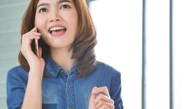 Asyalı kadınlar evdeki küçük ofis masasından akıllı telefon aracılığıyla konuşurlar. Genç Asyalı Kadın elleri telefon teknolojisi yaşam tarzını tutuyor. Mutlu kadın arayan kişi ev ofisinde dijital akıllı telefon kullanıyor.