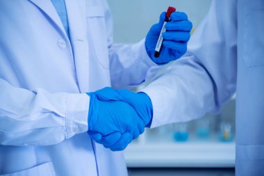 İki Asyalı bilim adamı takım arkadaşı el sıkışıyor. Kimya bilimi tüpü deneyi yapan araştırma görevlisi laboratuvarda biyoteknoloji antikor örneği tutuyor. Yakın plan şirket iş arkadaşı ortaklığı