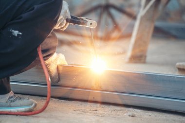 İnşaat işçisi elleri kaynak makineleri ile metal kıvılcımlar saçıyor. Erkek elleri koruyucu eldiven giyer. Alev metali, ateş demiri atölyesini keser. Çilingir kaynak makinesi kullanarak metal işlemini kesti