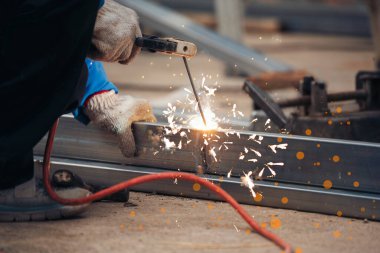 İnşaat işçisi elleri kaynak makineleri ile metal kıvılcımlar saçıyor. Erkek elleri koruyucu eldiven giyer. Alev metali, ateş demiri atölyesini keser. Çilingir kaynak makinesi kullanarak metal işlemini kesti