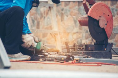 İnşaat işçisi elleri kaynak makineleri ile metal kıvılcımlar saçıyor. Erkek elleri koruyucu eldiven giyer. Alev metali, ateş demiri atölyesini keser. Çilingir kaynak makinesi kullanarak metal işlemini kesti