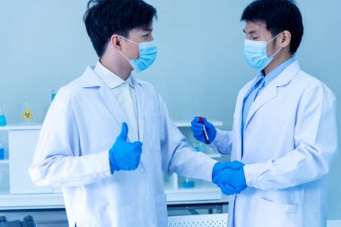 İki Asyalı bilim adamı takım arkadaşı el sıkışıyor. Ekin Adamlar kimya bilimi tüpü deneyi örneklerini laboratuvarda tutuyor. El ve kurumsal ortaklığı kapatın.
