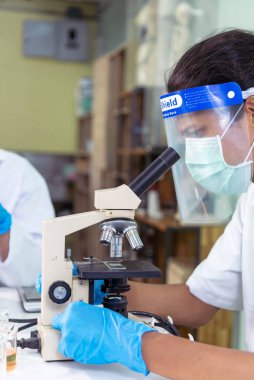 Indian Scientist man look into Microscope research in science laboratory. Asian biochemistry scientist using microscope in laboratory chemistry labs. Covid-19 medical research scientific experiment